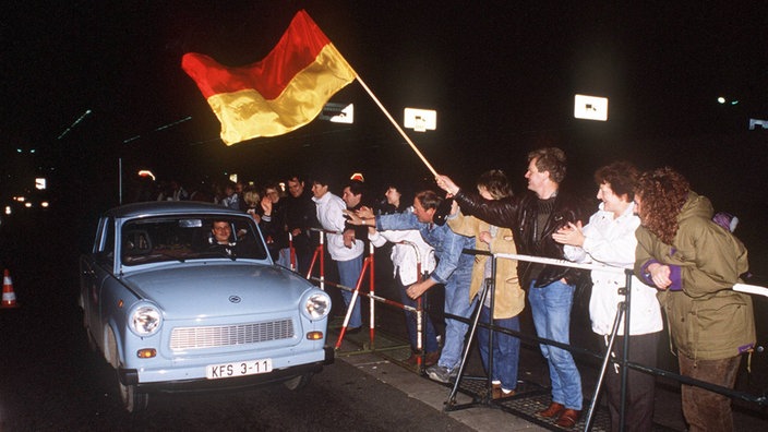 Ein Trabant fährt an jubelnden Menschen vorbei