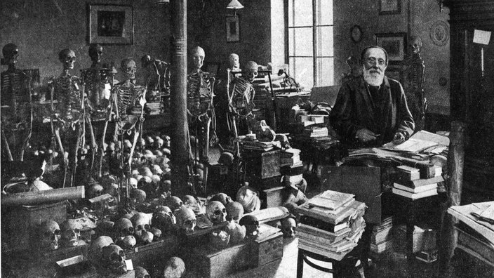 Umgeben von Skeletten steht der Mediziner Rudolf Virchow in seinem Arbeitszimmer in Berlin