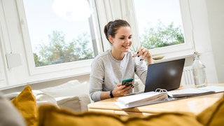 Eine Frau sitzt an einem Couchtisch und blickt auf ihren Laptop