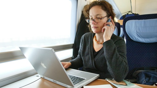 Eine junge Frau sitzt in einem Zug der Deutschen Bahn und arbeitet an ihrem Laptop.