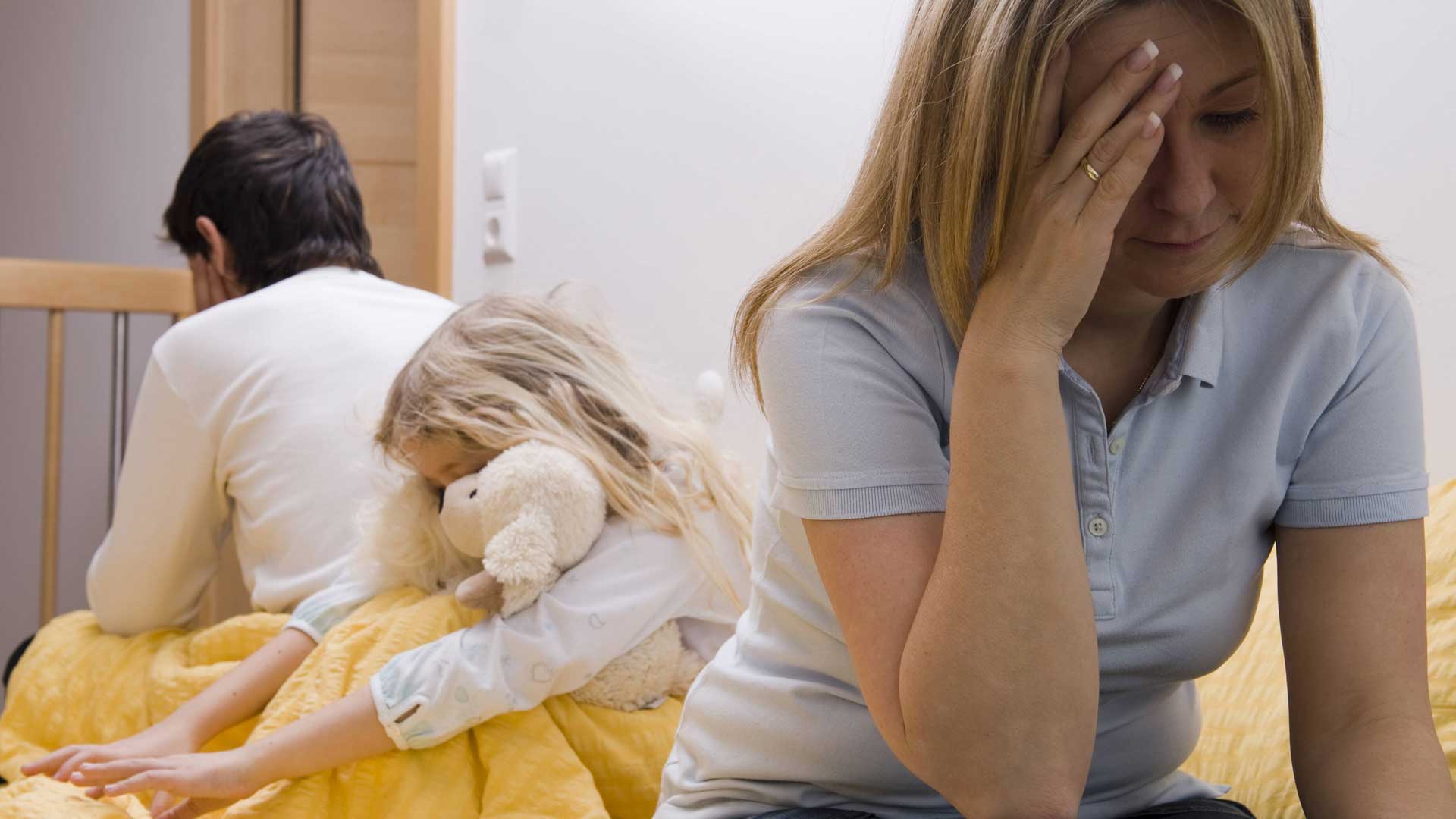 Die Eltern haben sich den Rücken zugekehrt. Das Kind sitzt im Hintergrund und hält seinen Teddy fest umschlungen.