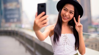 Eine junge Frau mit Hut lächelt und macht ein Selfie