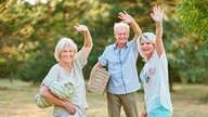 Drei Senioren stehen winkend im Park