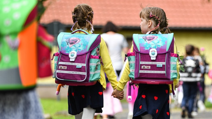 Zwillingsmädchen Hand in Hand mit gleichen Schulranzen 