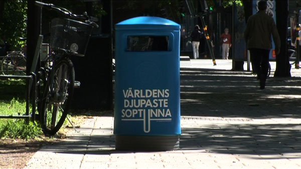 Blauer Mülleimer auf einem Gehweg.