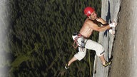 Ein Mann mit Kletterausrüstung klettert eine Steile Wand hoch.