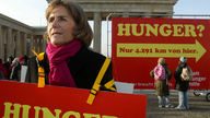 Eine Frau hält vorm Brandenburger Tor ein Protestplakat hoch. Auf dem Plakat steht das Wort Hunger.