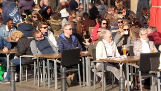 Menschen sitzen auf Stühlen auf einem öffentlichen Platz.