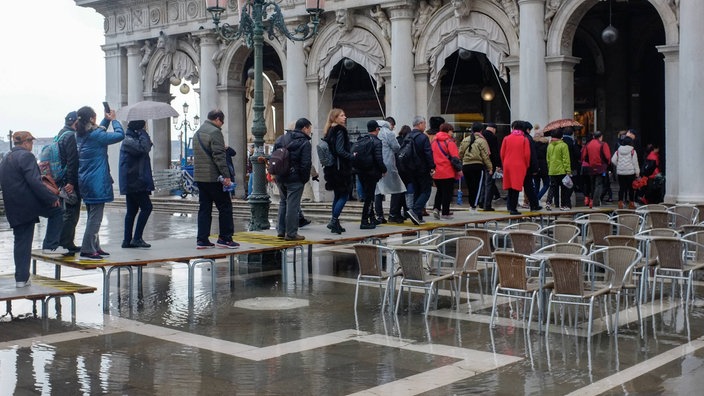 Menschen gehen auf einem Steg über einen überfluteten Platz