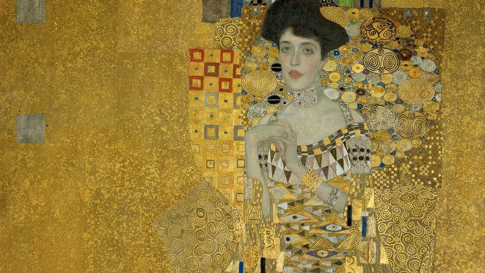 Gemälde von Gustav Klimt: Eine verführerische dunkelhaarige Frau mit einem reich verzierten Kleid vor goldenem Hintergrund.