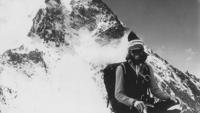 Das Schwarzweiß-Bild zeigt rechts Reinhold Messner, kaum zu erkennen mit Sonnenbrille und einer gestreifte Mütze, kinnlangem Haar und Vollbart