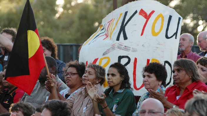 Eine Gruppe westlich gekleideter Aboriginal-Frauen mit Flagge bei Kundgebung.