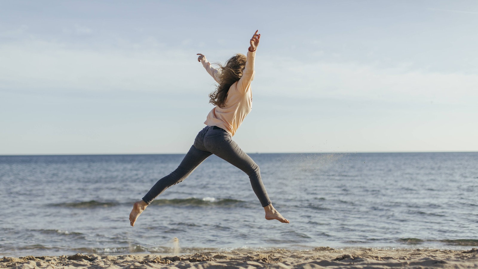 Eine Frau macht Luftsprünge am Strand 