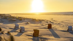 Sonnenuntergang am langen Sandstrand von Juist, an dem einige Strandkörbe stehen