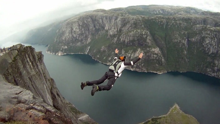 Basejumper kurz nach dem Absprung in der Luft über einem tiefen Fjord.