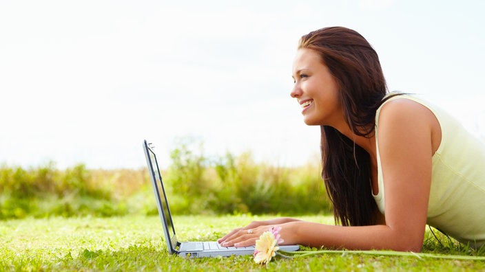 Frau mit Laptop, auf einer Wiese liegend