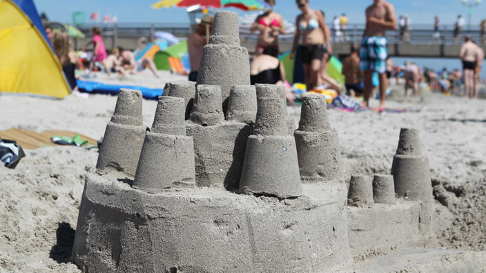 Eine kleine Sandburg inmitten einer bunten Strandszene in Grömitz, Schleswig-Holstein.